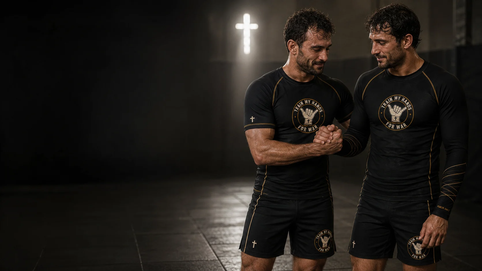 Two training partners in black TMHFW rashguards and shorts clasping hands mat-side